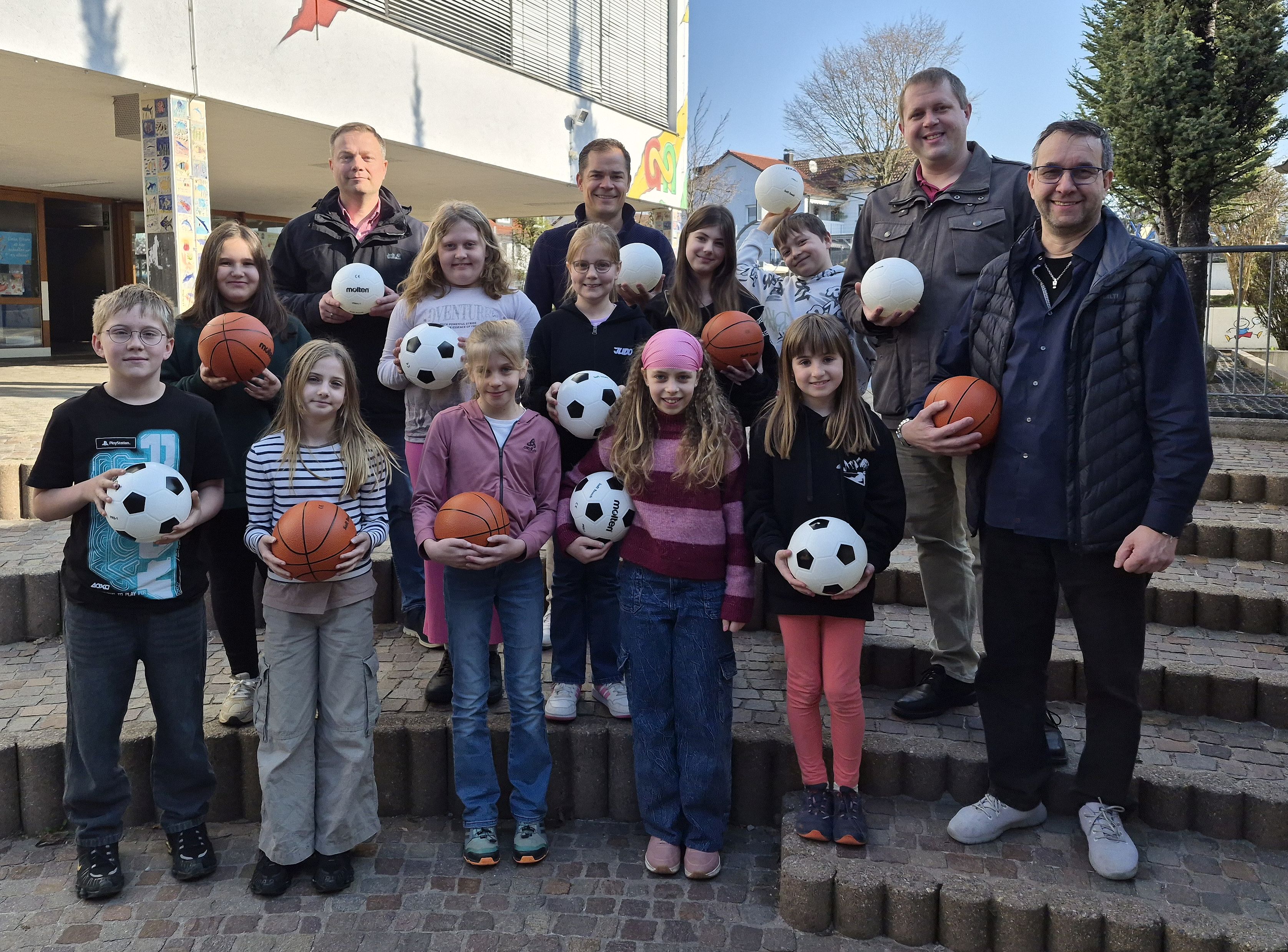 Foto mit 3 Fördervereinsmitgliedern, Rektor Stefan Vetter und einingen Kindern; alle haben verschiedene Bälle in der Hand